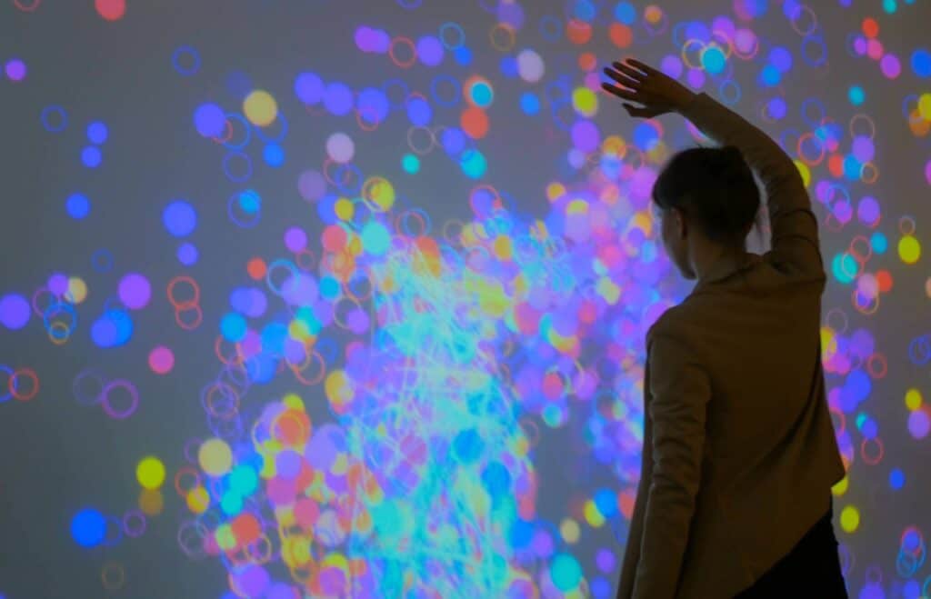 Image shows a person in a room withlights on the wall showing a network. The person is reaching for the lights