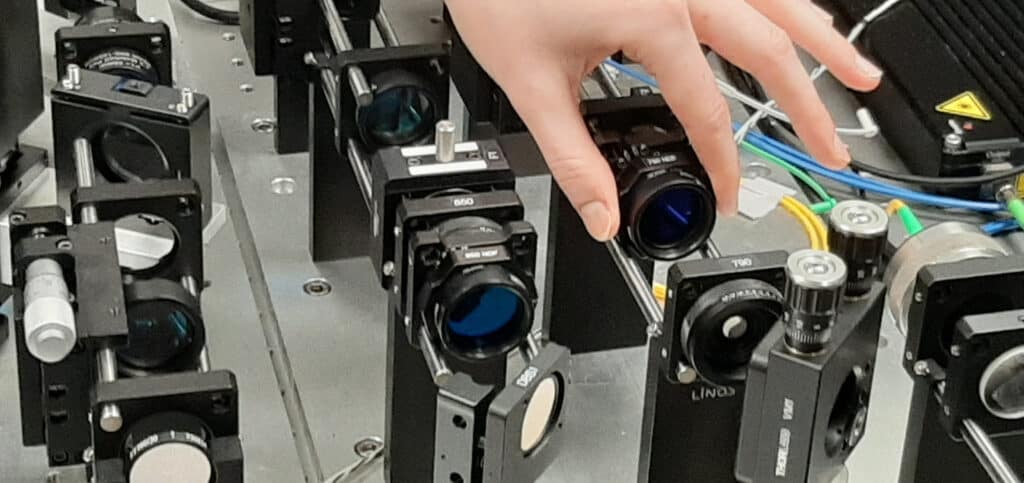 Image shows a hand moving a lens inside a machine with many lenses and mirrors