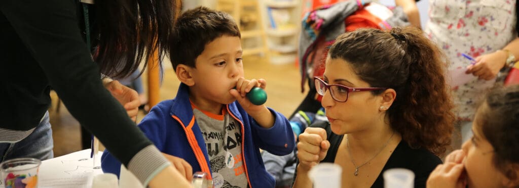 Image shows two people one child left and a woman right. The child is blowing up a small balloon. The place is busy. It is a science festival based on eyes.