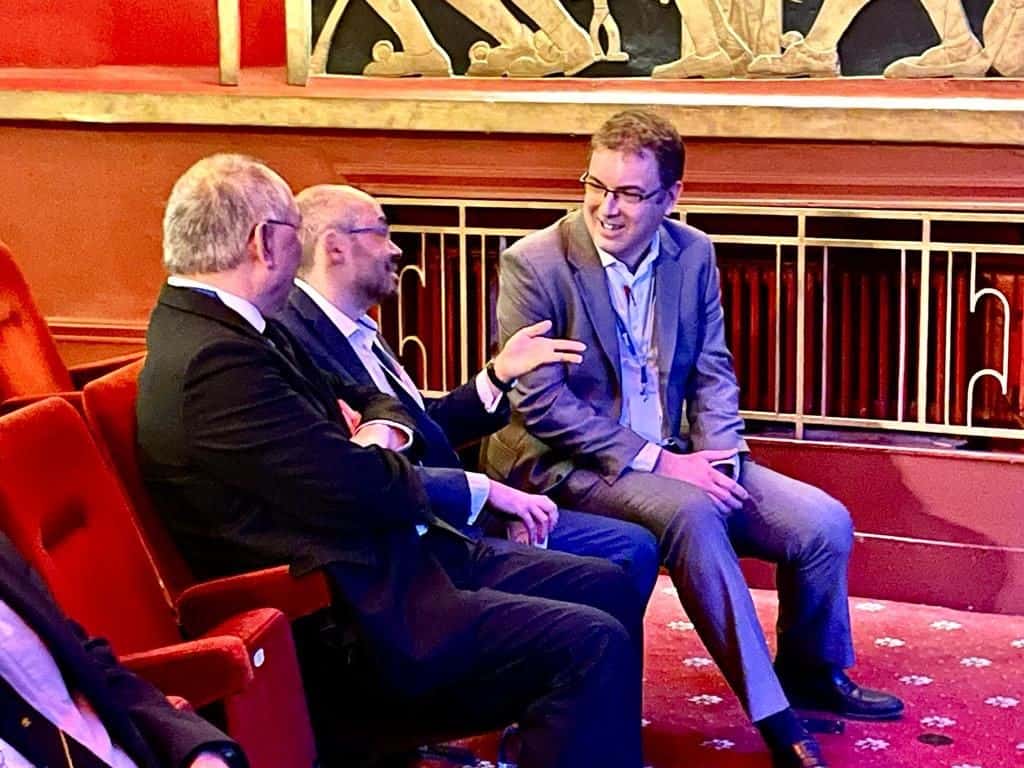 Three individuals chatter, gesture and smile.