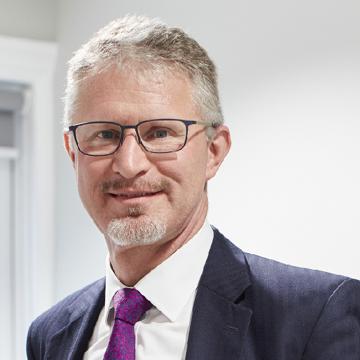 A headshot of Prof Paul Foster. Paul is wearing a suit and glasses and smiling at the camera.