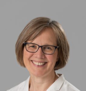 Image shows Annegret, on a grey background a white lady with a light bob and a white blouse.