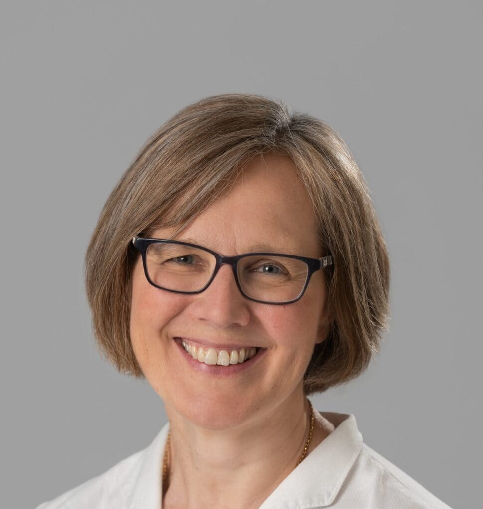 Image shows Annegret, on a grey background a white lady with a light bob and a white blouse.