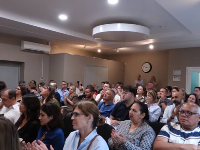 Crowd watch a talk and clap hands in a large room.