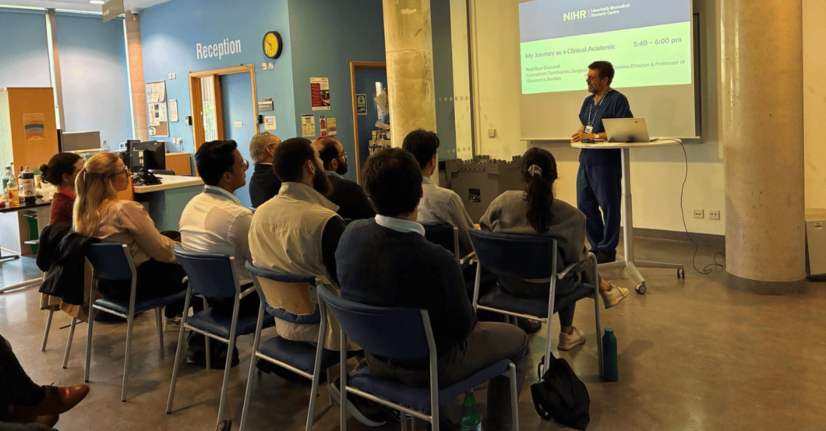 Clinical trainees seated in a hospital reception area listen to a speaker presenting slides titled “My Journey as a Clinical Academic” at an NIHR Moorfields Biomedical Research Centre event.