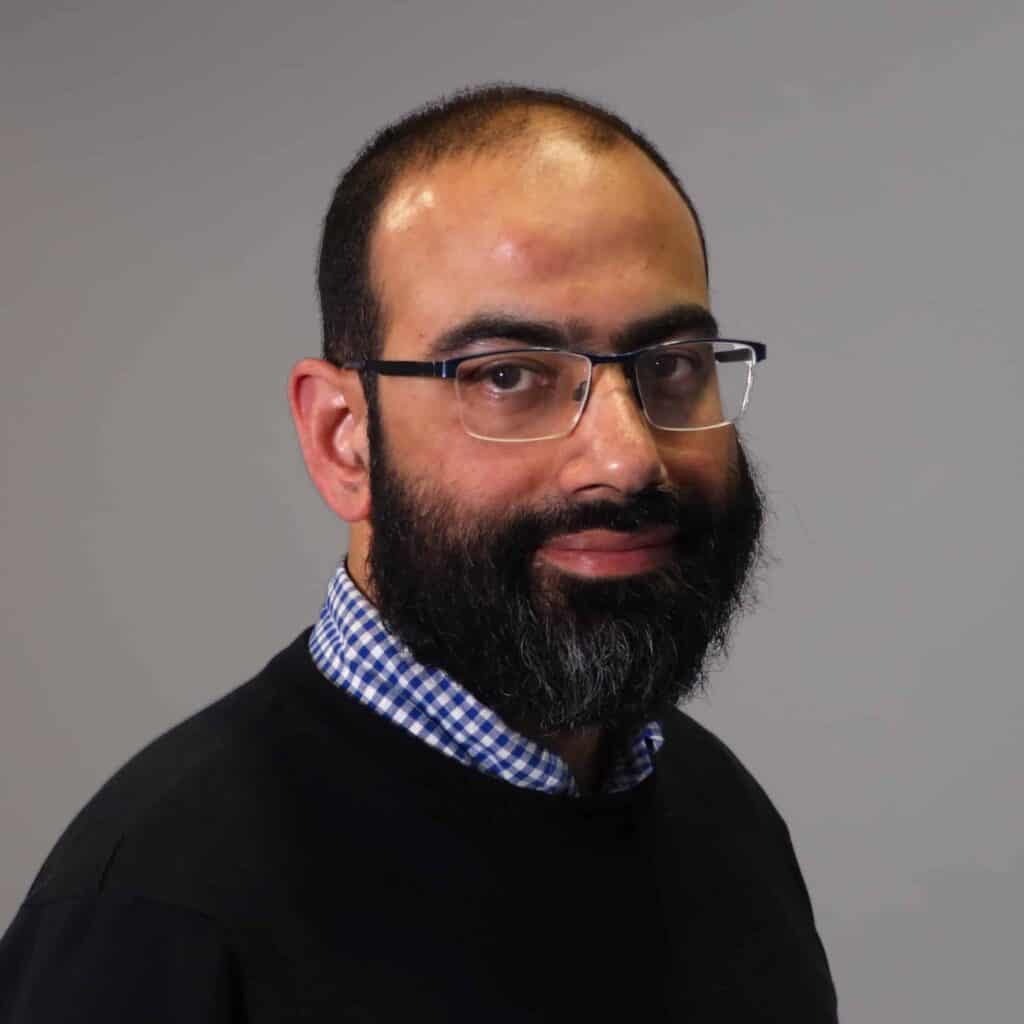 A headshot of Prof. Omar Mahroo wearing a black sweatshirt over a blue-and-white checkered shirt.