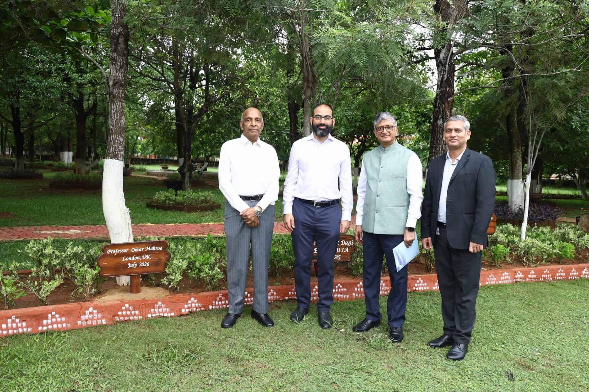 Four men stand in front of a tree in a garden area, one is Prof. Mahroo, a plaque near the tree reads Professor Omar Mahroo, London, July, 2026