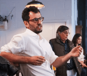 individual in a white shirt with glasses gesticulates